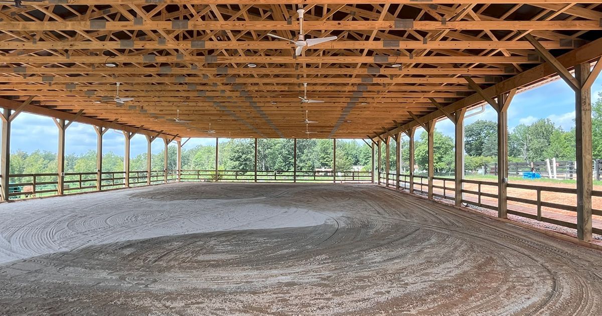 Covered riding arena with tan sand and wooden structure.