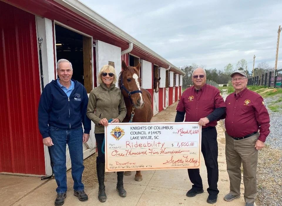 Group presents a large check to a woman with a horse. Red barn backdrop.