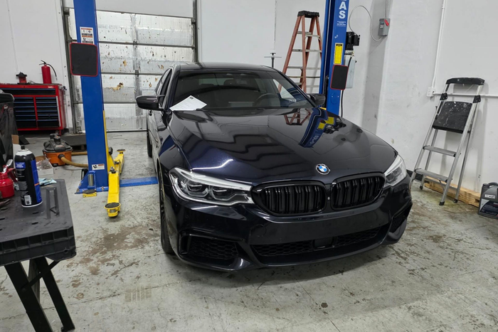 Black BMW sedan in an auto shop bay with car lift and tools in the background | DFW Auto Repair