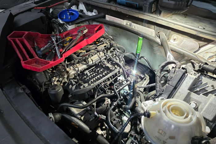 Car engine under repair with red tool tray and blue funnel in a dim garage | DFW Auto Repair