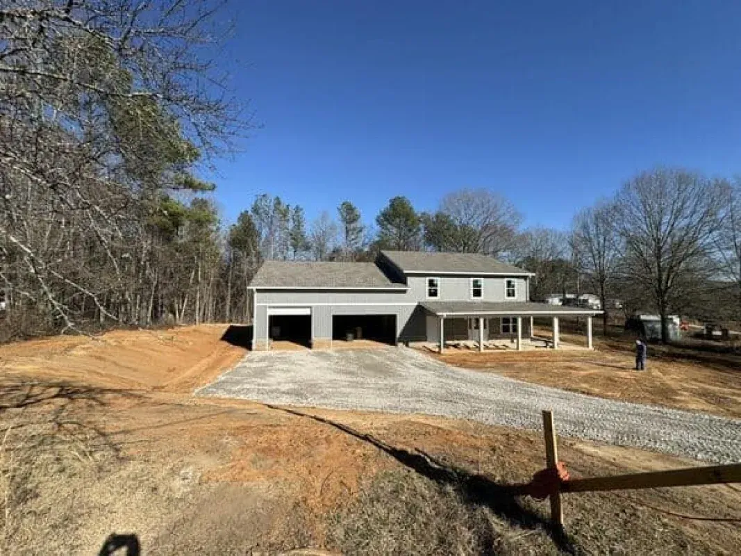A two-story grey house with a garage and covered front porch, surrounded by bare trees and dirt landscaping.