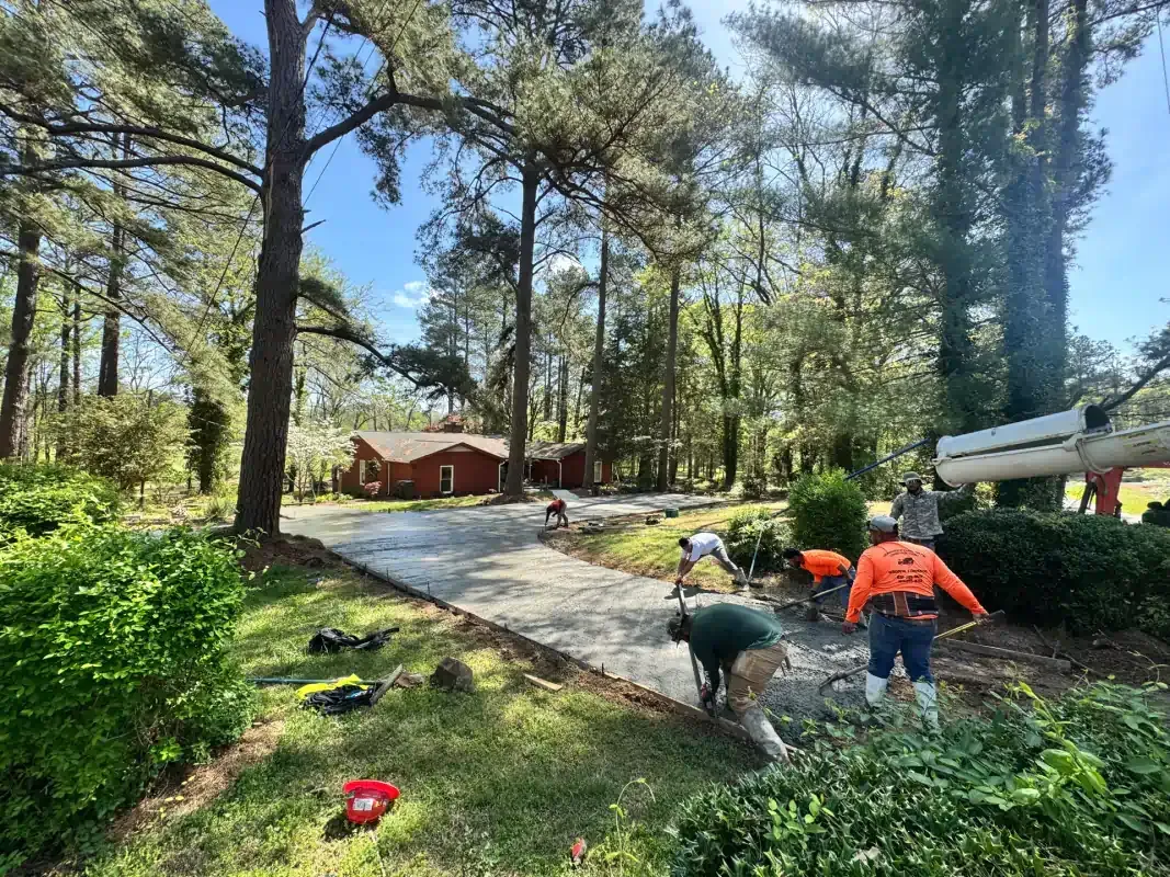 Workers use a concrete pump to pour a new driveway in a wooded residential area.