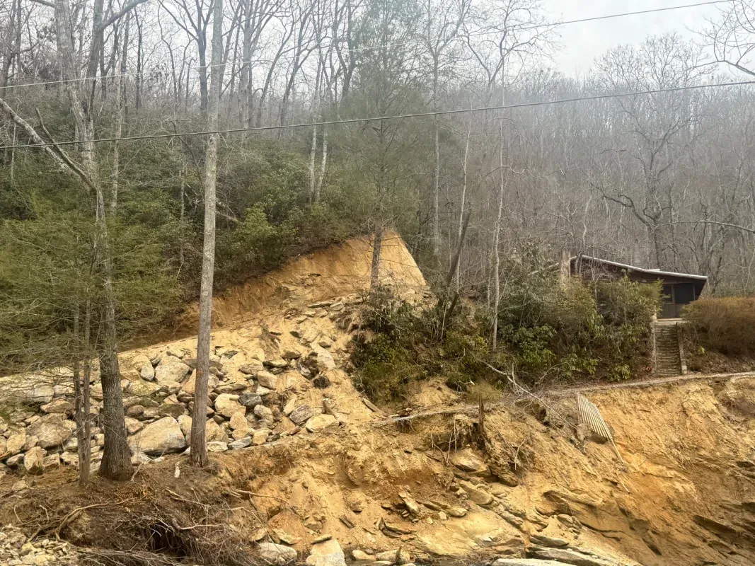 A hillside showing signs of a recent landslide, with exposed dirt, scattered rocks, and damaged vegetation.
