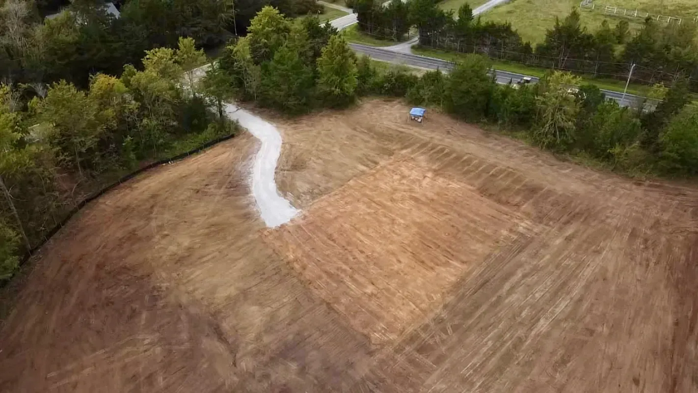 An aerial view of a cleared construction site with a gravel driveway leading to a graded square building pad.