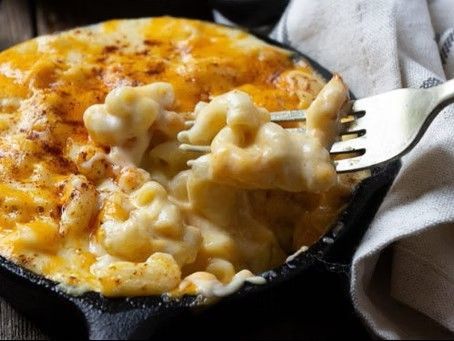 Cheesy baked macaroni and cheese in a skillet, with a fork lifting a creamy bite