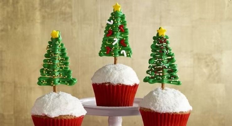 Christmas tree cupcakes topped with white frosting and green tree decorations on a stand