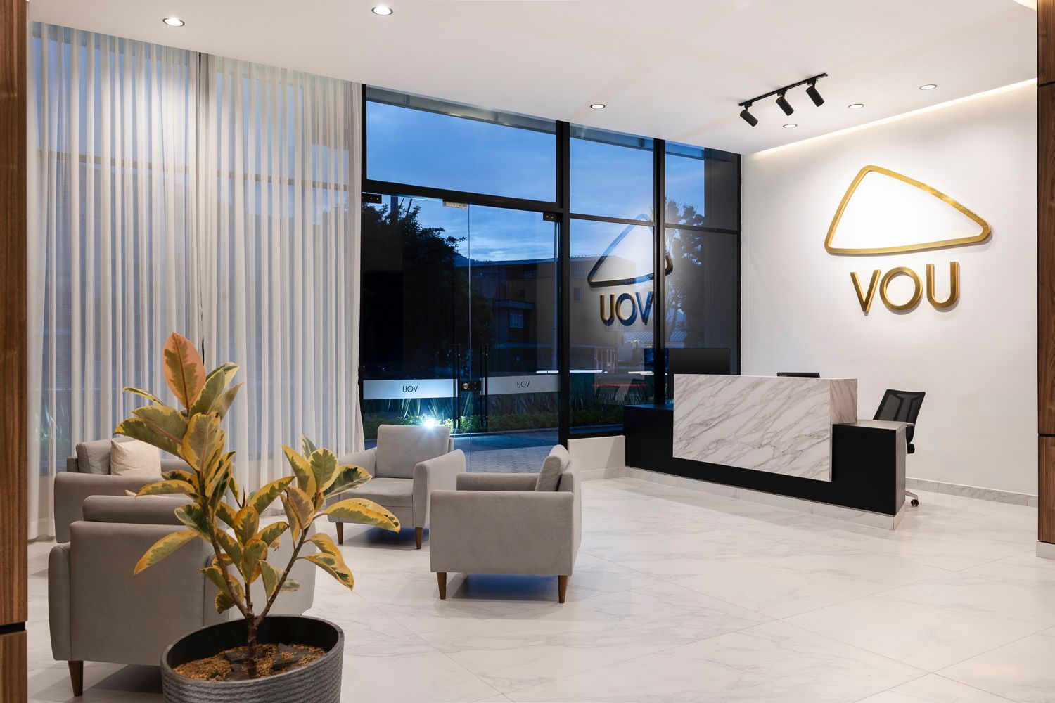 Recepción con sillones grises y el logo luminoso de VOU, un hotel para viaje de negocios