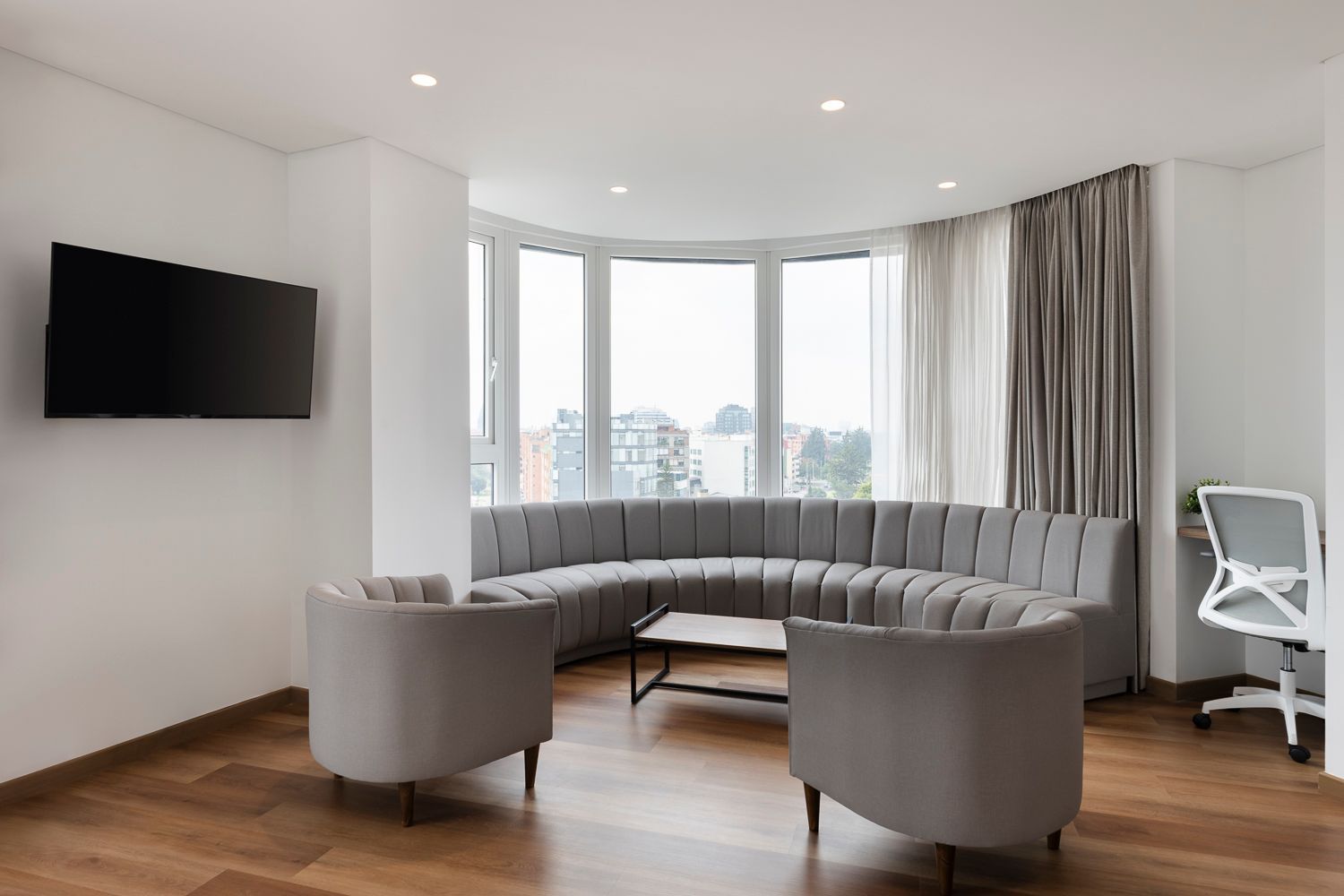 Sala de estar con un sofá curvo gris y ventanas amplias en VOU suites, de mejores hoteles para ejecutivos