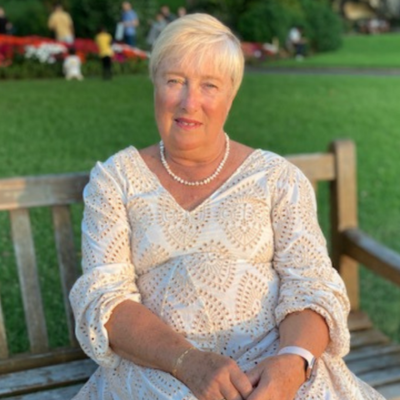 Carol, Tutorio qualified primary school teacher-tutor, seated on a park bench in a white patterned dress
