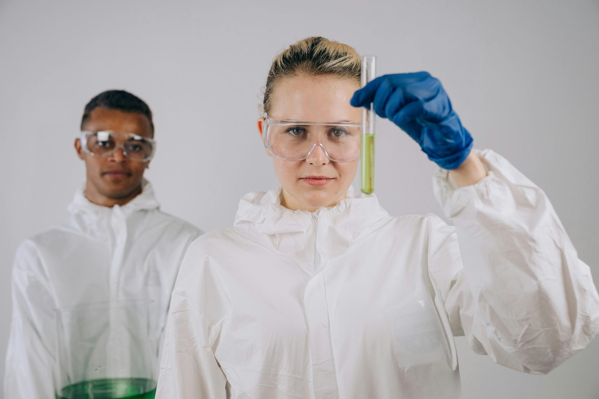 Two scientists in white lab coats, one holding a test tube with blue gloves in a lab setting.