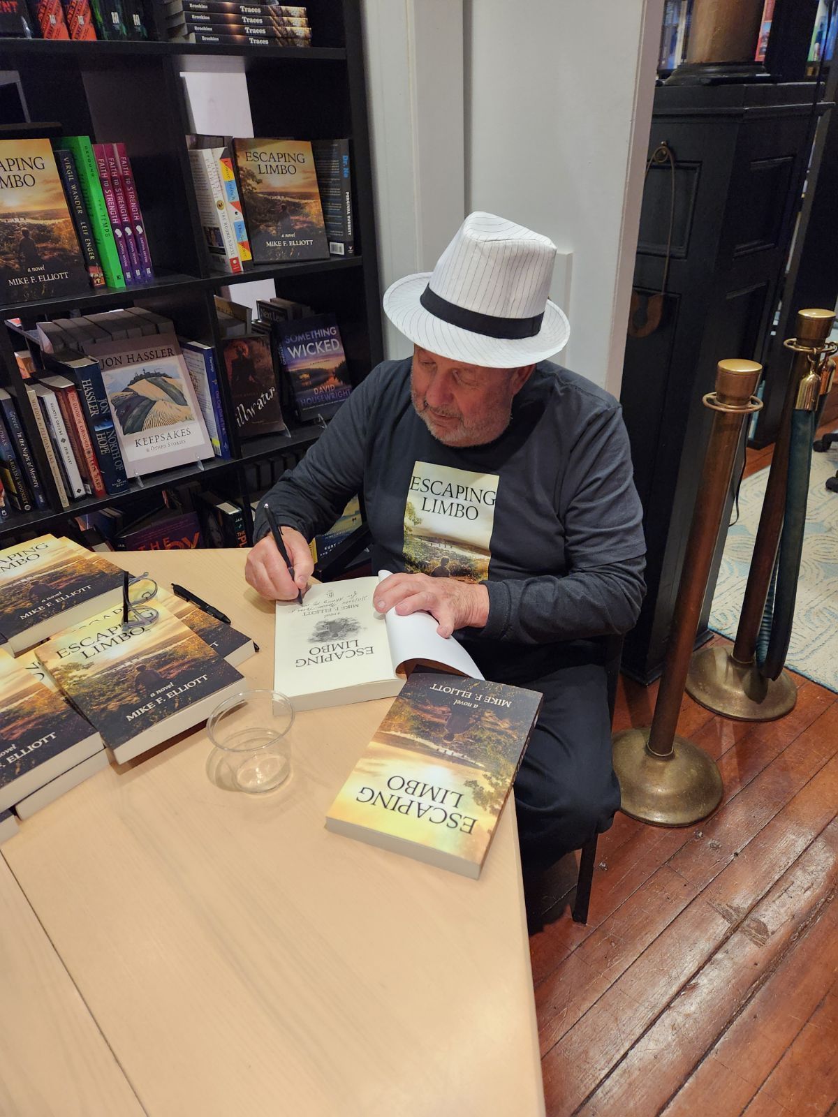 Man in white hat signing books at a table in a bookstore.