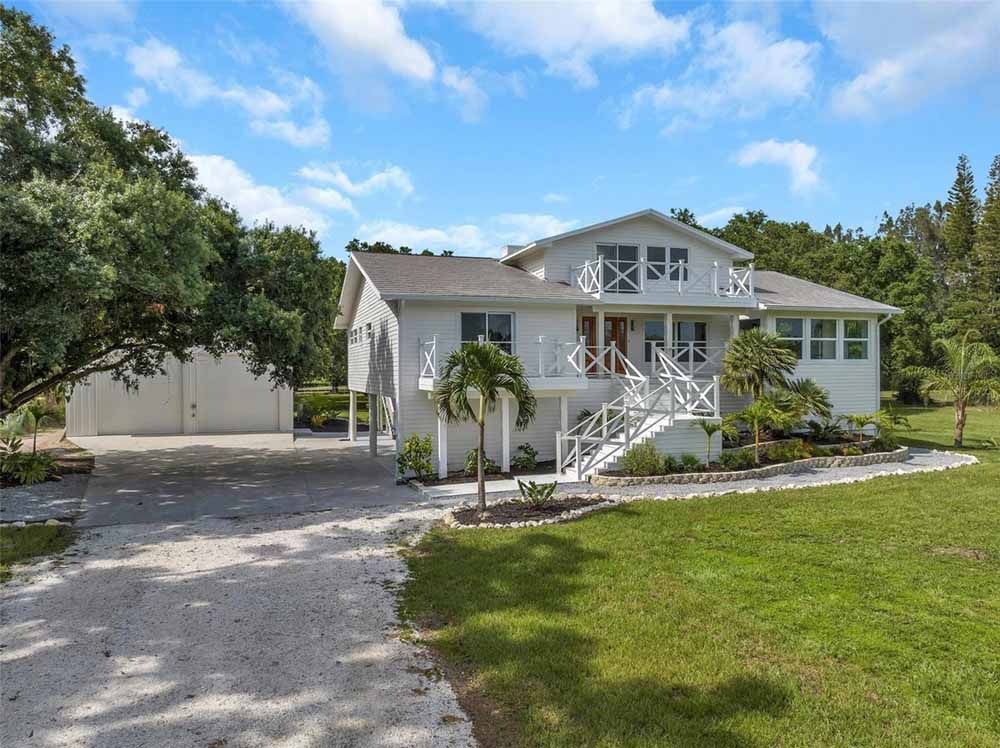 White two-story house with a white bridge and driveway on a grassy lot under a blue sky.