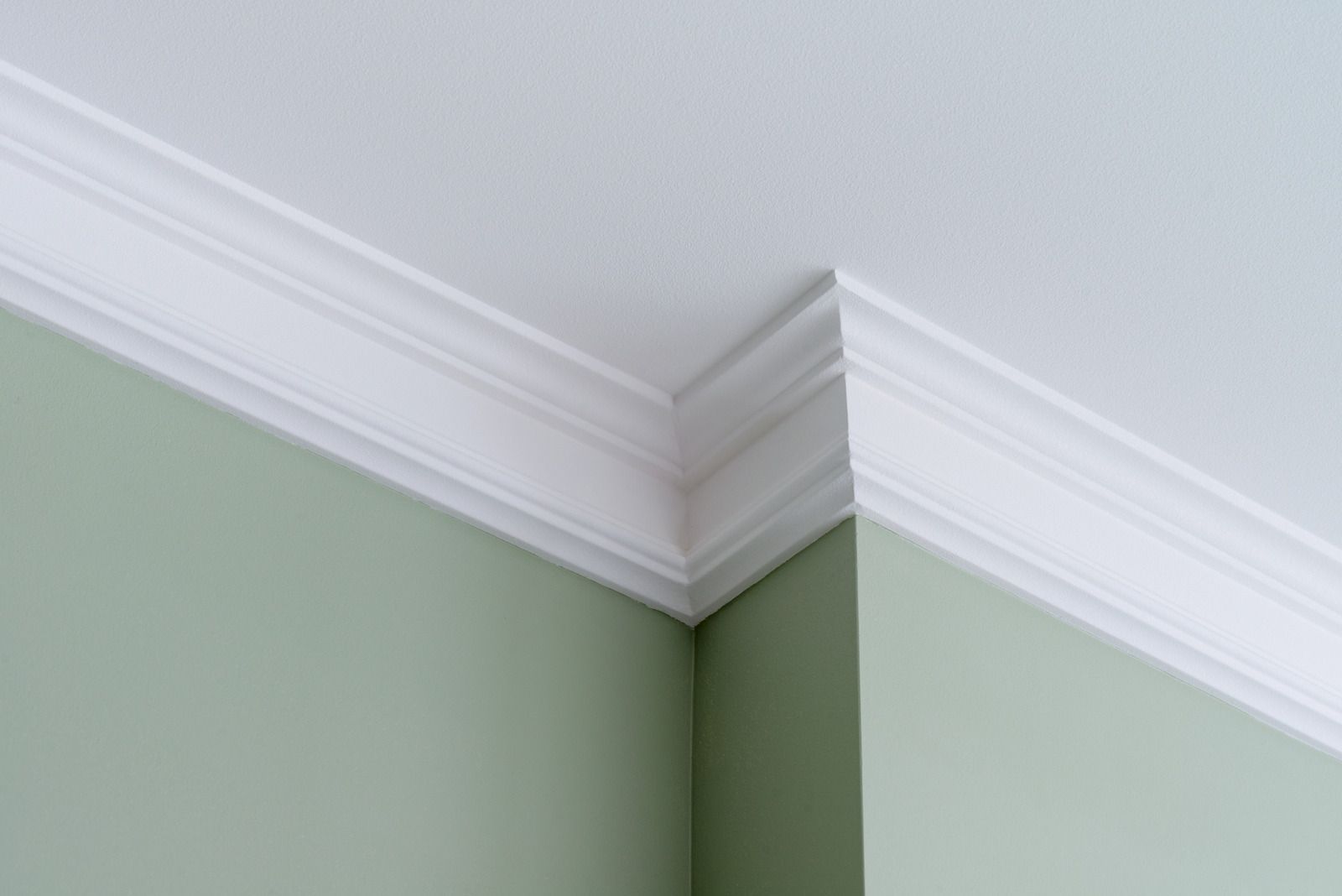 Corner of a room with white crown molding and pale green walls meeting at the ceiling