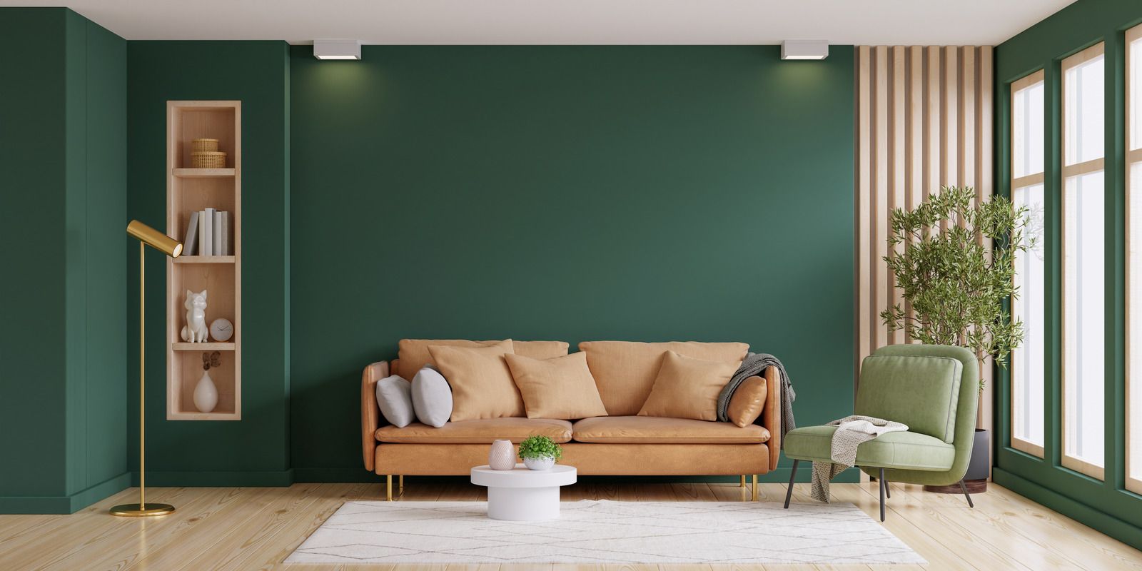 Modern living room with green walls, tan sofa, green armchair, wood shelves, and large windows