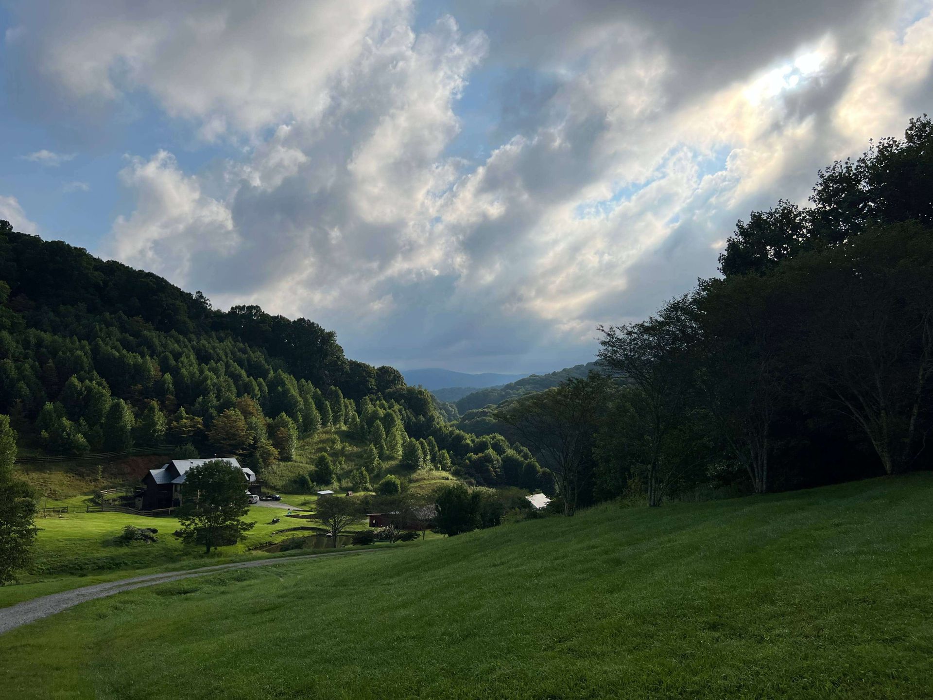 Green valley under a cloudy sky, with forested mountains and sunlight breaking through.