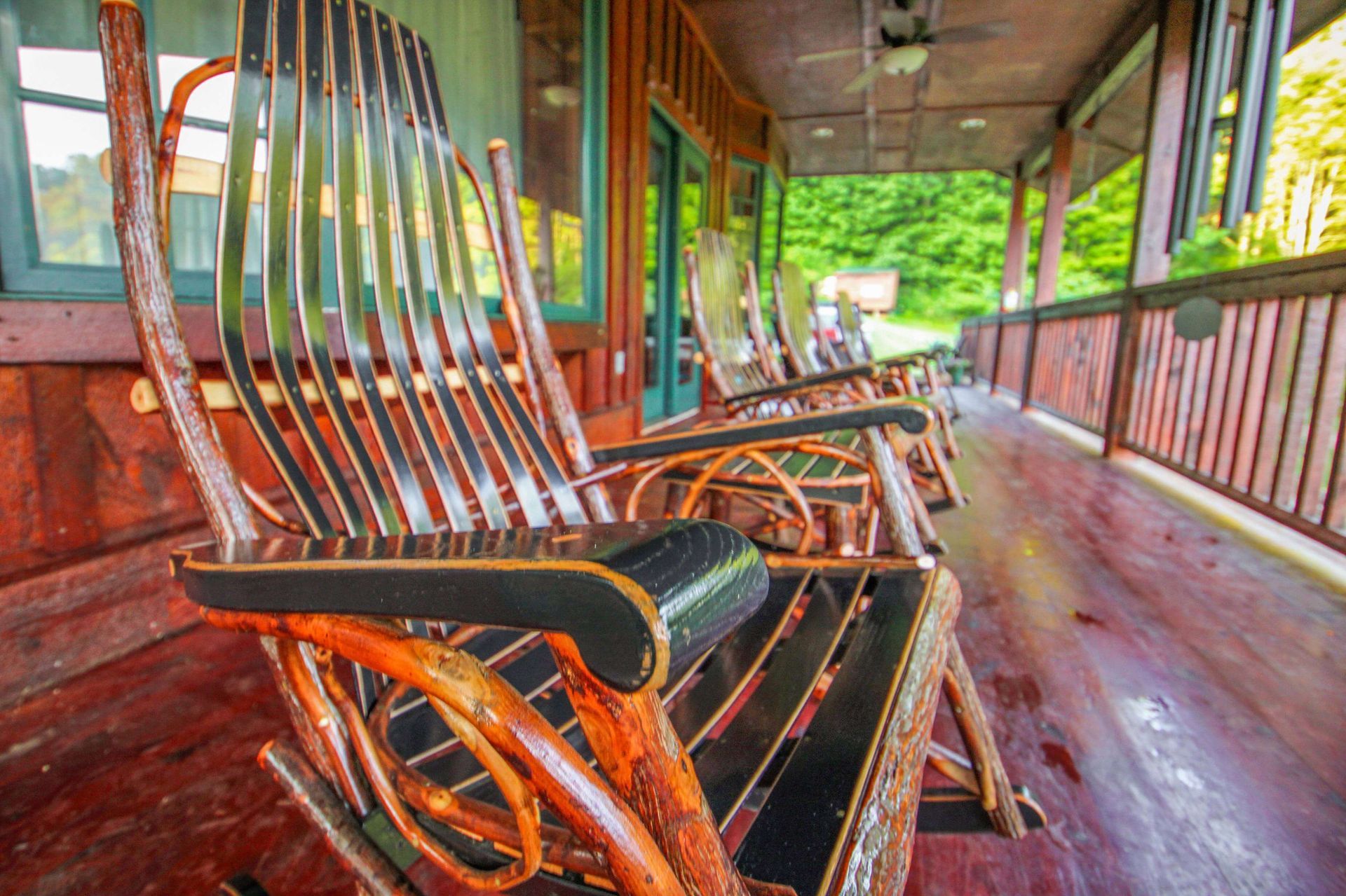 Wooden rocking chairs on a porch, facing a green, outdoor view.