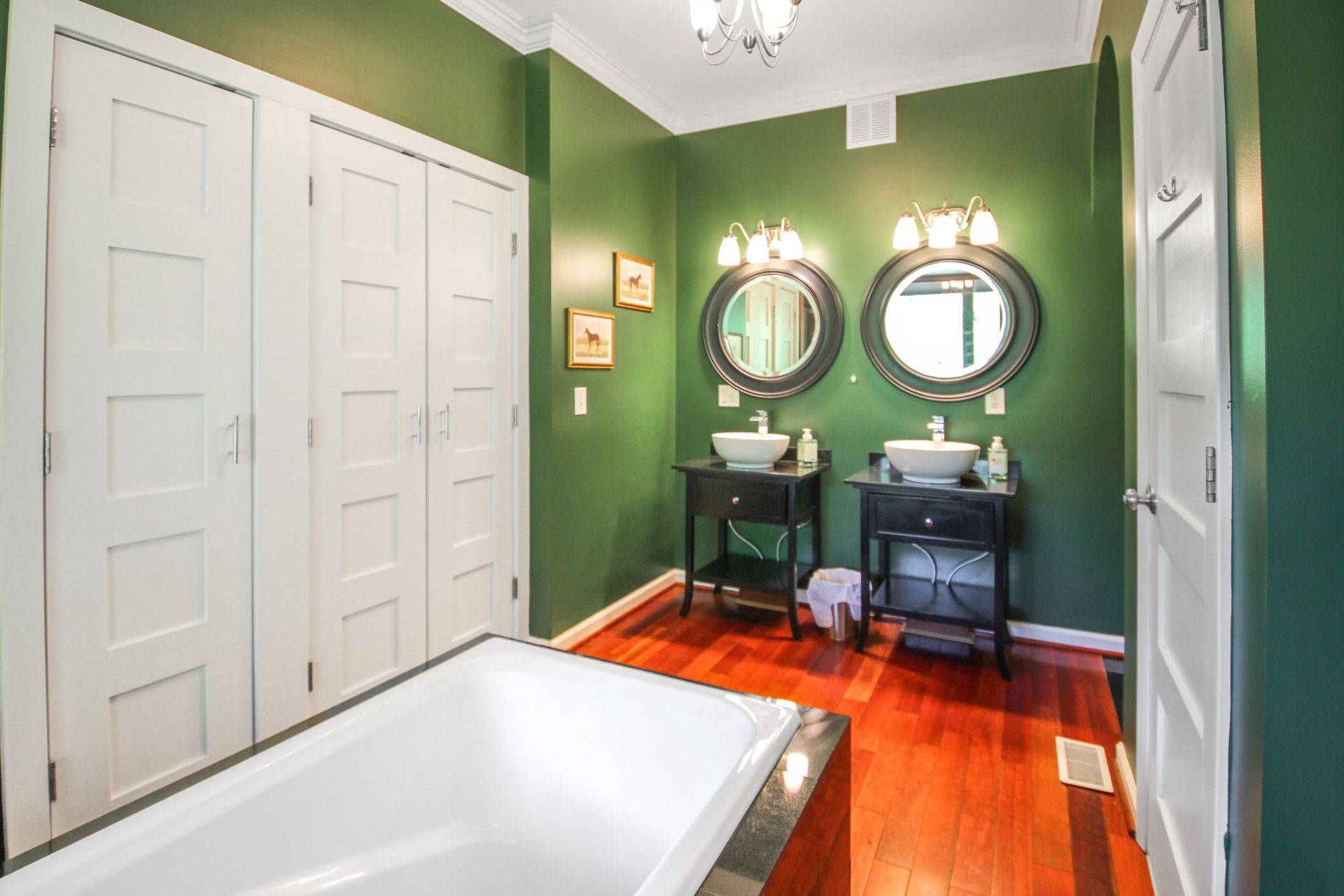 Green bathroom with white cabinets, two sinks with mirrors, and a bathtub.