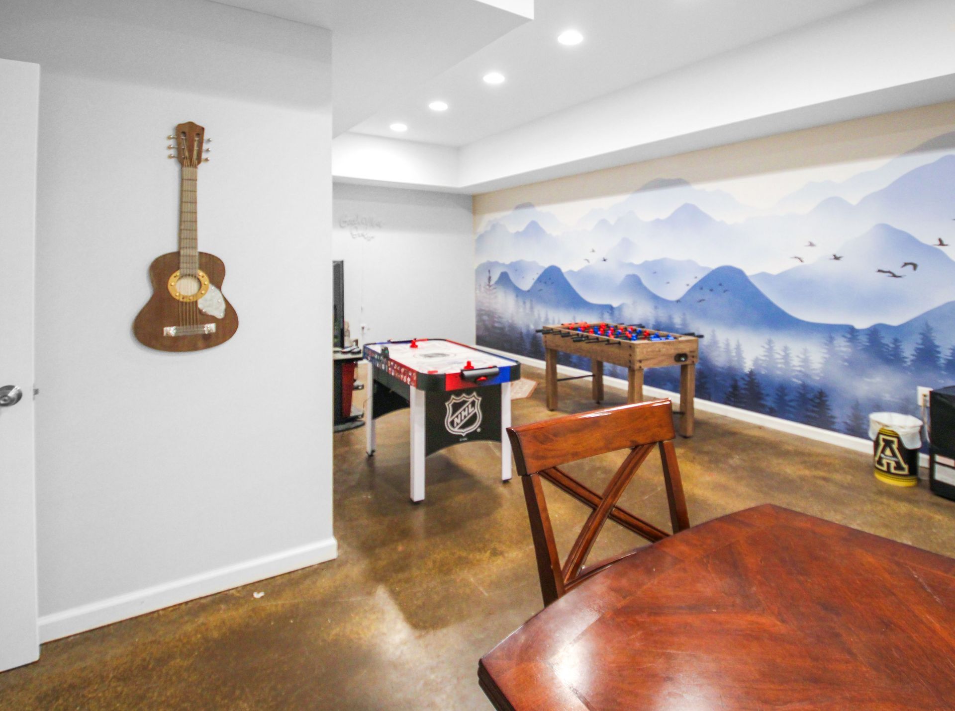 Basement game room with foosball, hockey table, guitar, and blue mountain mural.