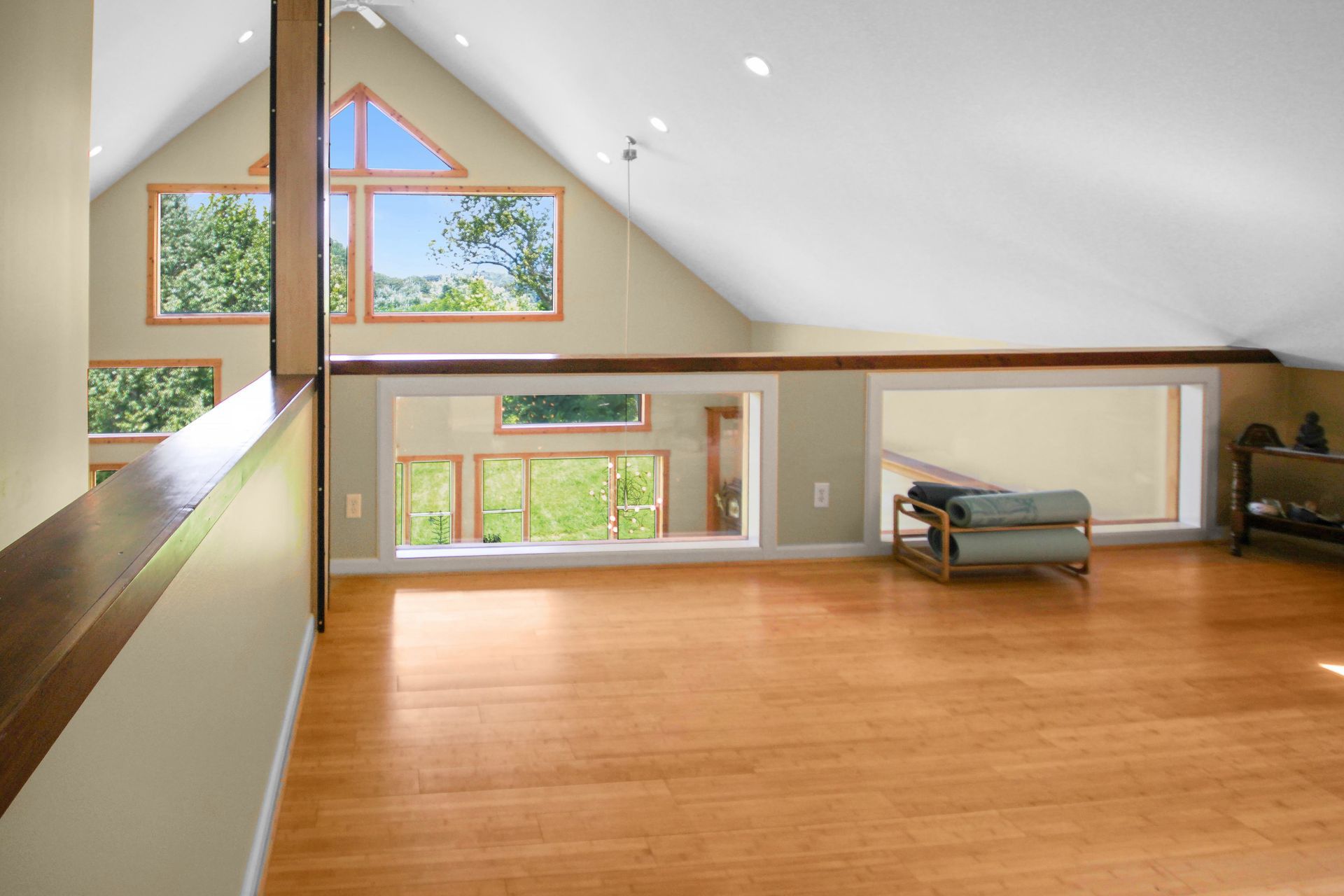 Bright loft with wood floors and multiple windows, overlooking a scenic view of green trees.