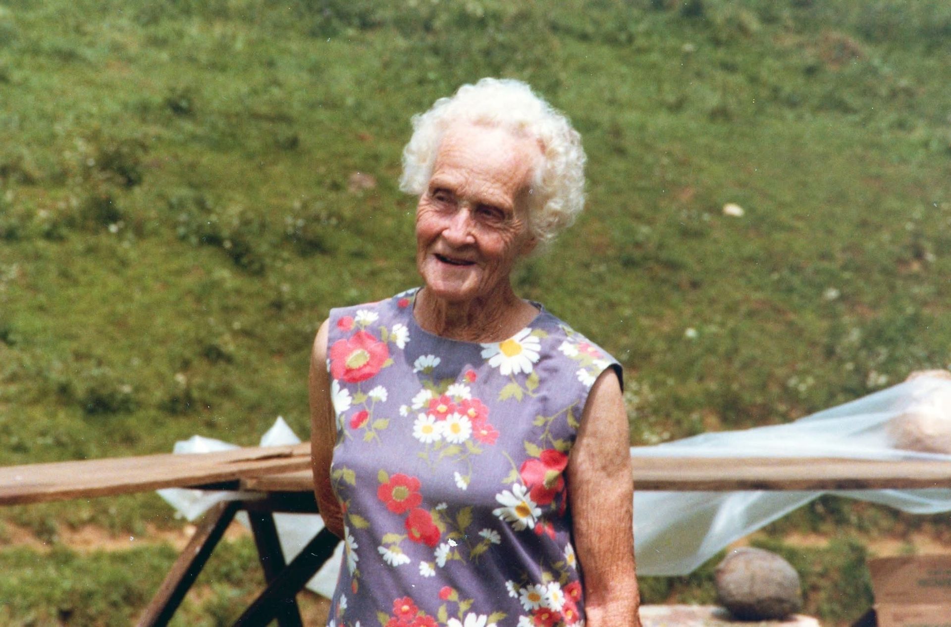 Elderly woman in floral dress smiles outdoors.