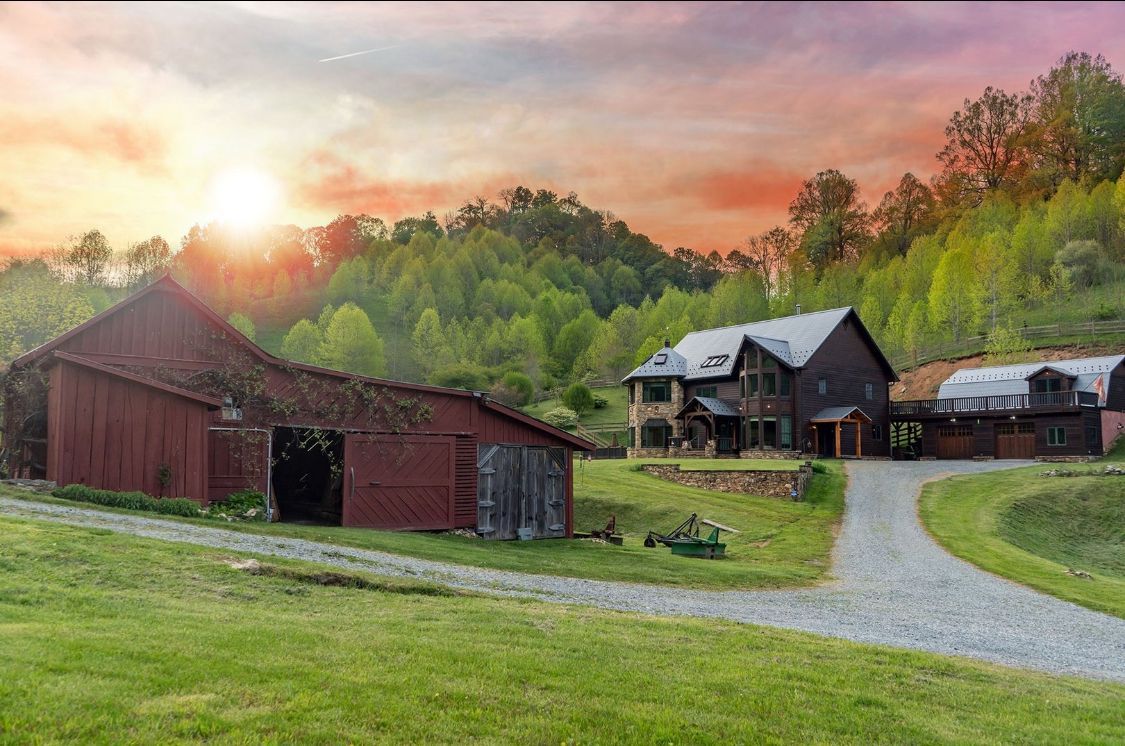 Red barn and house on a green hillside with a gravel drive at sunset.