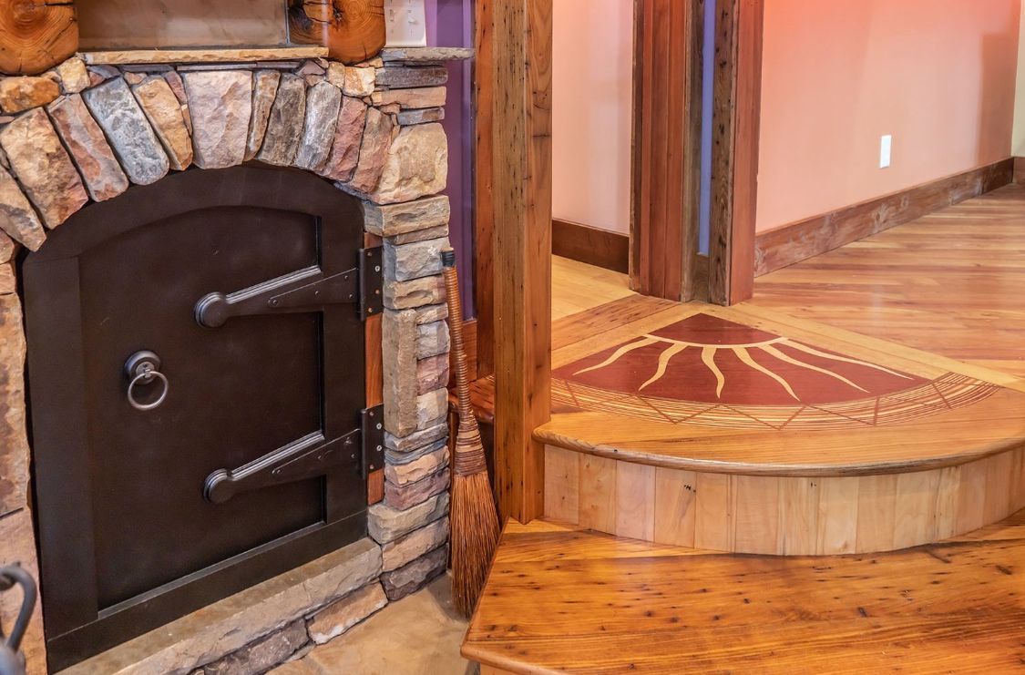 Stone-framed iron door, next to a wooden floor with inlaid sun design and wood pillar.