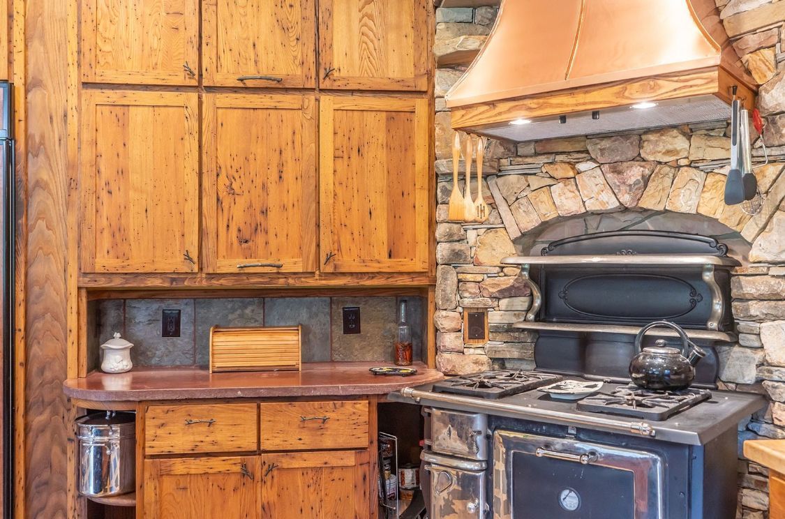 Kitchen with wooden cabinets, a stone arch around the stove, and copper range hood.