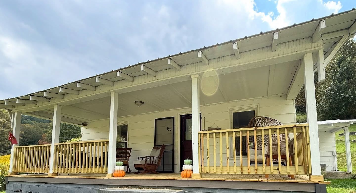 White house with a long wooden porch and railing under a cloudy sky.