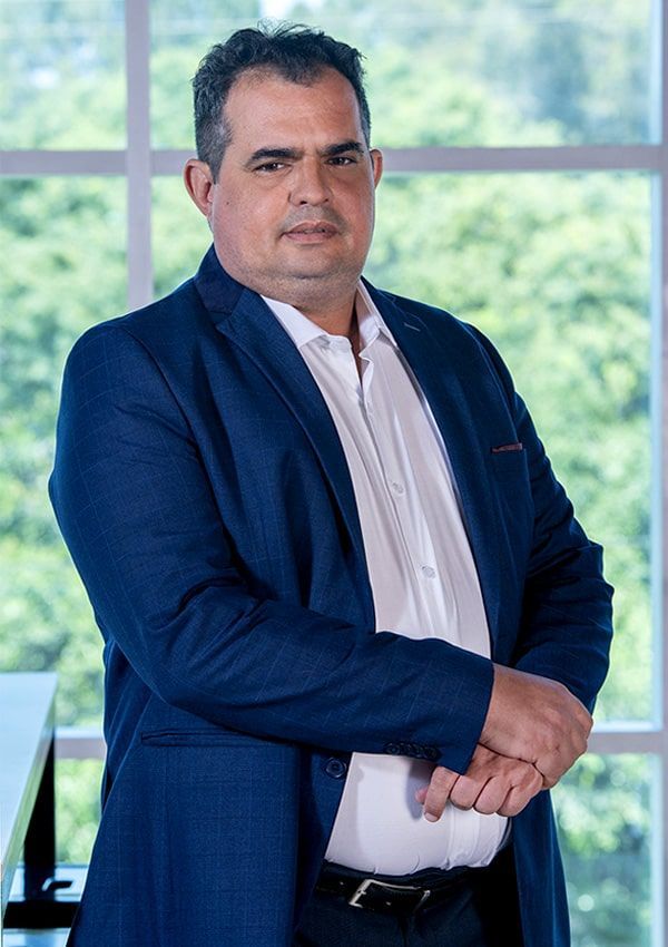 Un hombre con traje azul y camisa blanca está parado frente a una ventana.