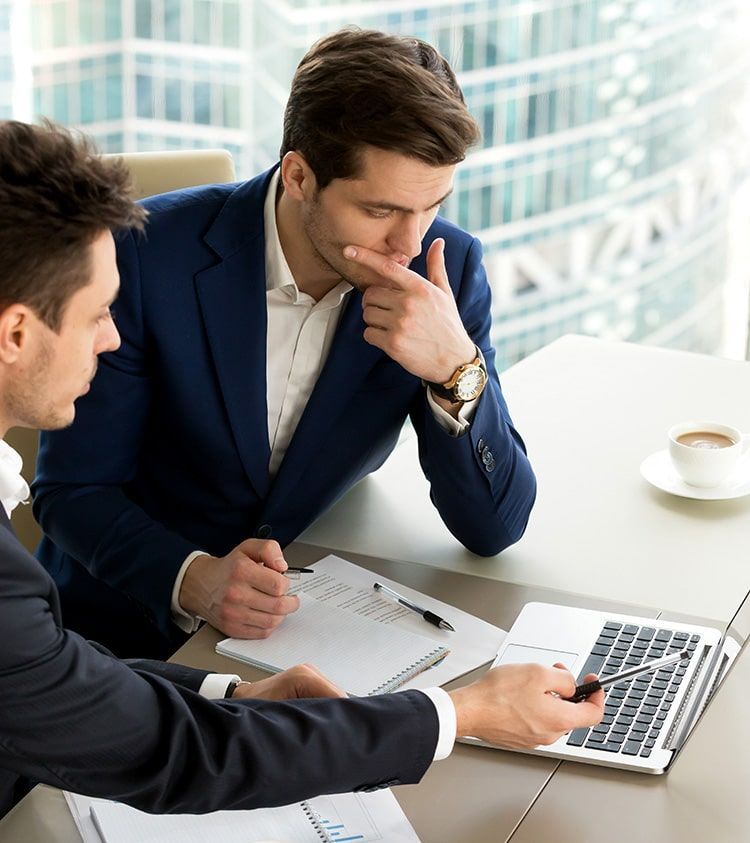Dos hombres están sentados en una mesa mirando una computadora portátil.
