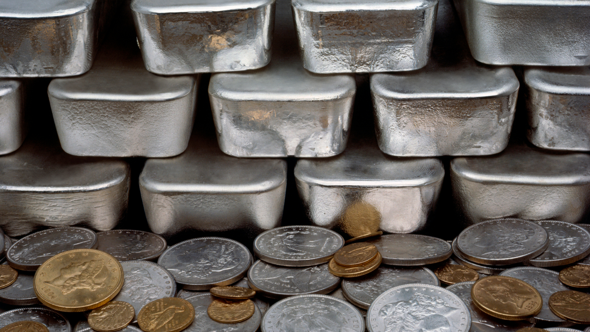 Stacked silver bars and mixed coins arranged in rows on a dark surface