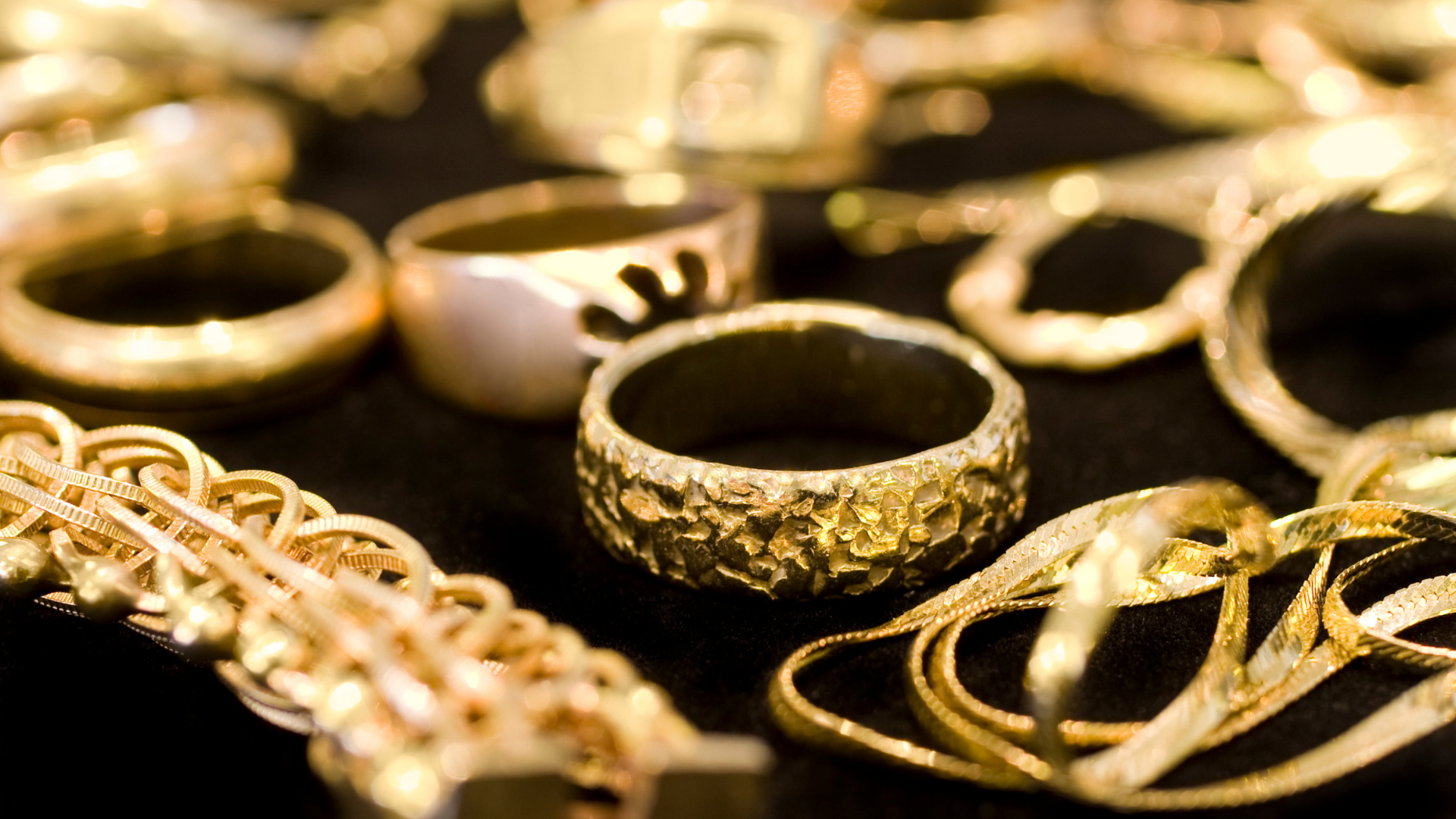 Assorted gold rings and chains arranged on a dark surface, close-up.