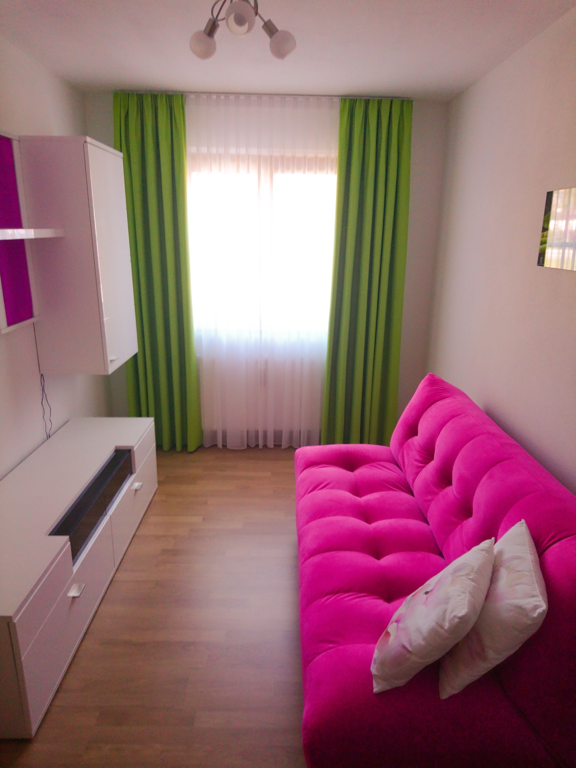 Ein Wohnzimmer mit einem rosa Sofa und grünen Vorhängen