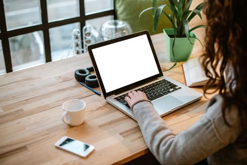 Stock photo of a woman using a laptop, with a cup of coffee and a phone also on her desk