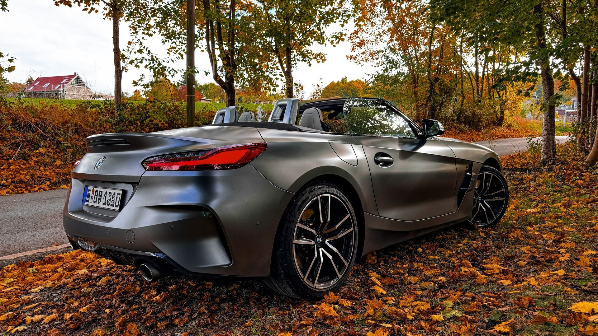 Gray convertible sports car parked on an autumn leaf-covered road among trees
