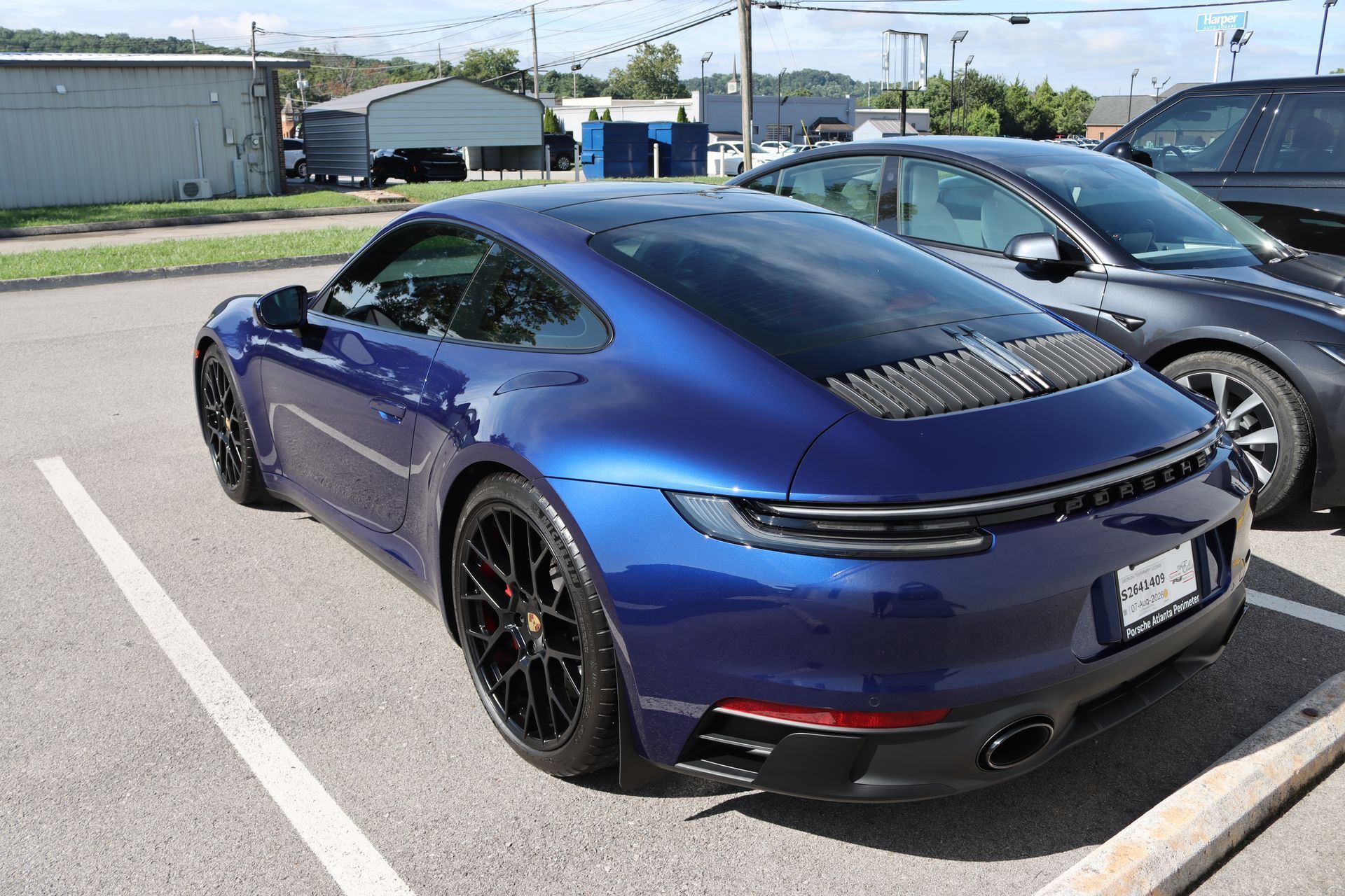 Blue Porsche 911 parked in a lot, rear three-quarter view with black wheels and spoiler trim