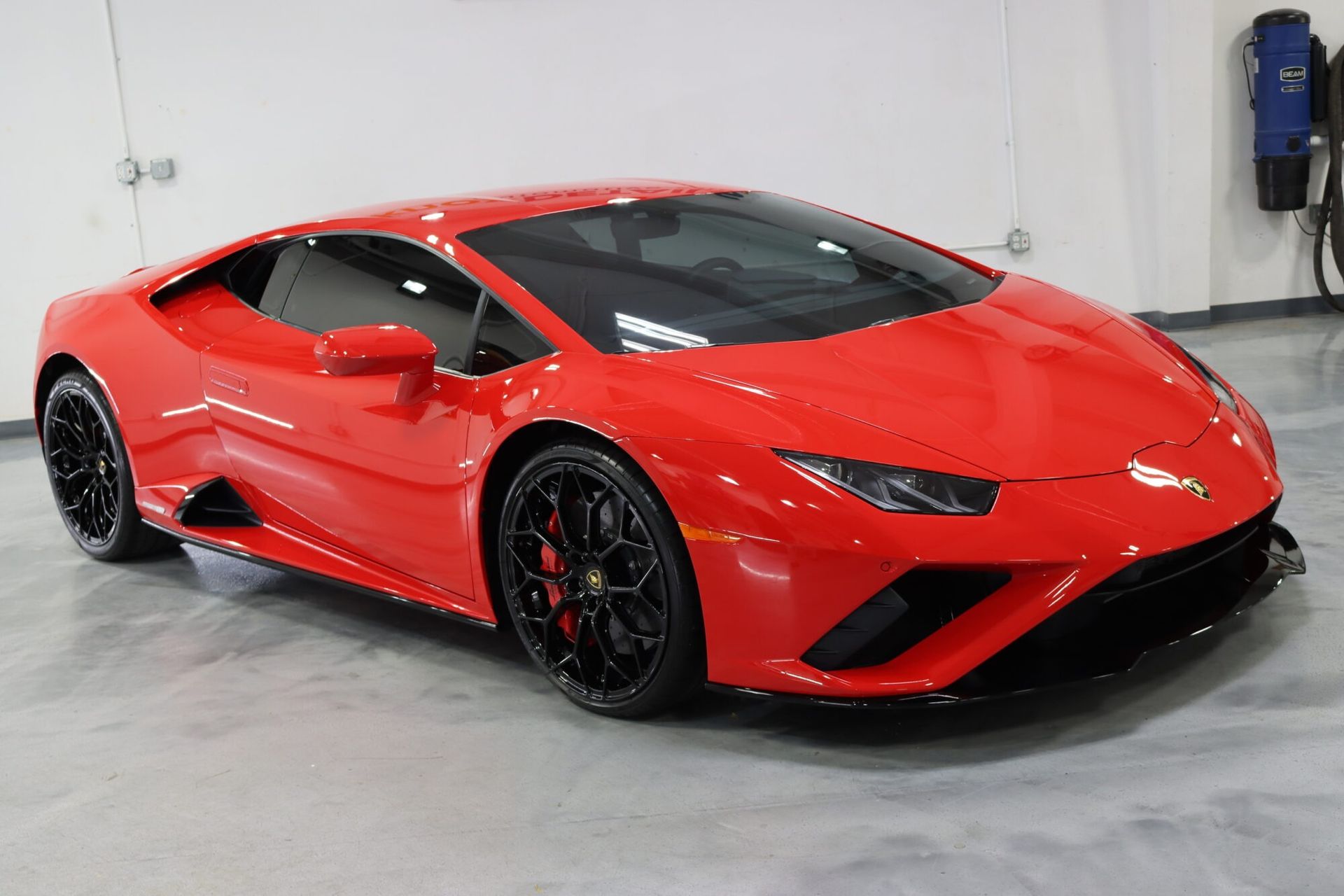 Red sports car in a white garage, viewed from the front-left side.