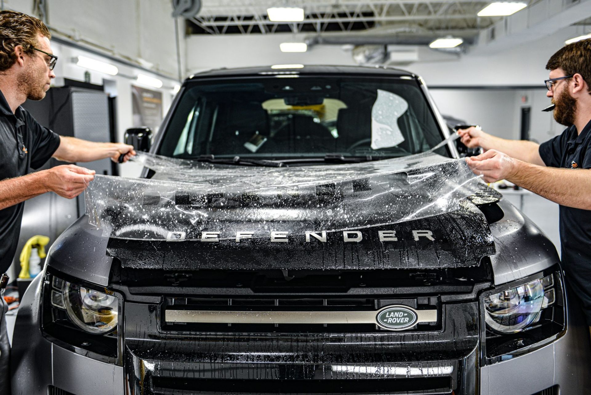 Two people wrapping a black SUV in a bright auto workshop