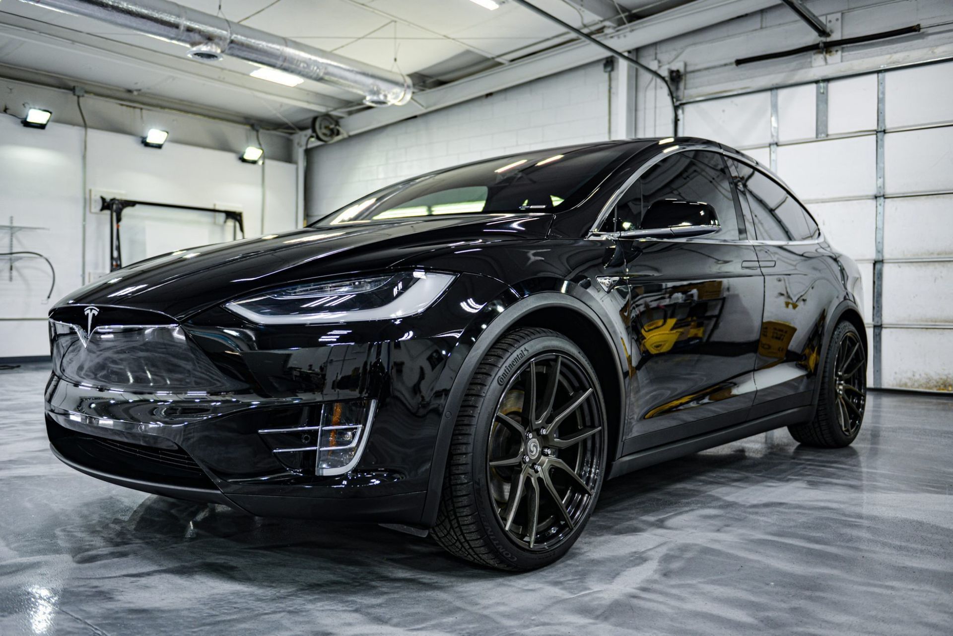 Black Tesla SUV parked in a bright garage, angled front view with black wheels