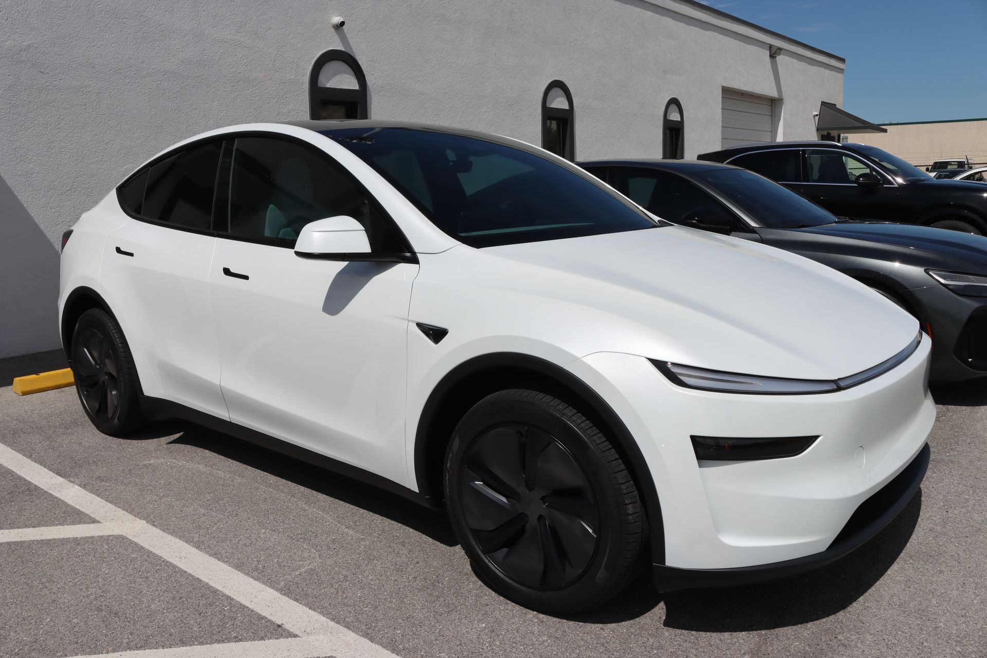 White Tesla Model Y parked in a lot beside another car, viewed from the front-left side.
