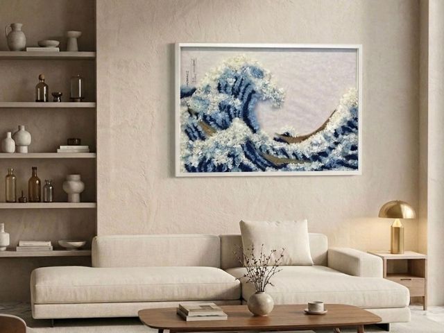 Soggiorno dai toni neutri con divano color crema, tavolino da caffè in legno e un quadro raffigurante un'onda blu sopra di esso.