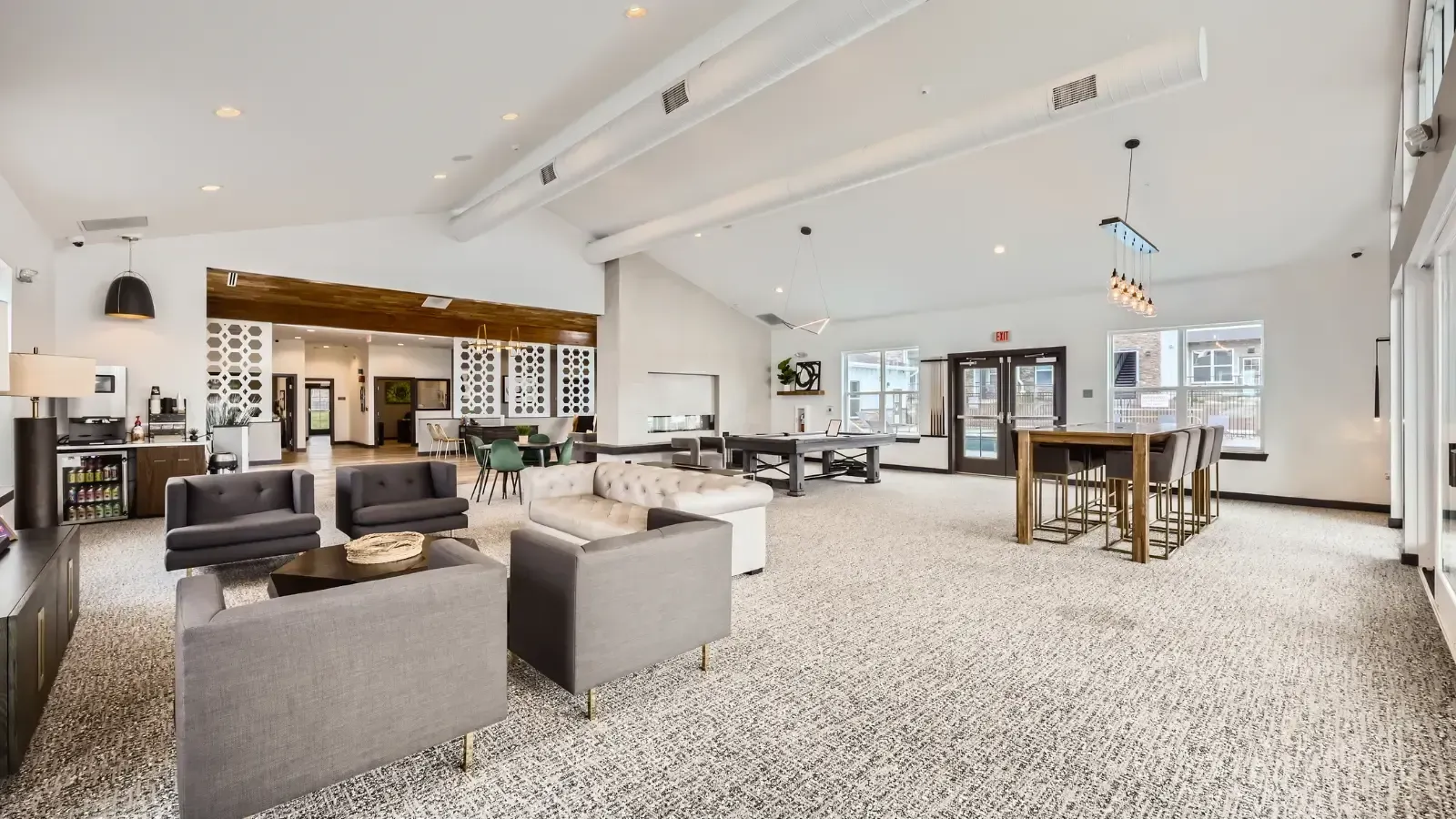 Open-concept community lounge with gray seating, tables, and large windows.