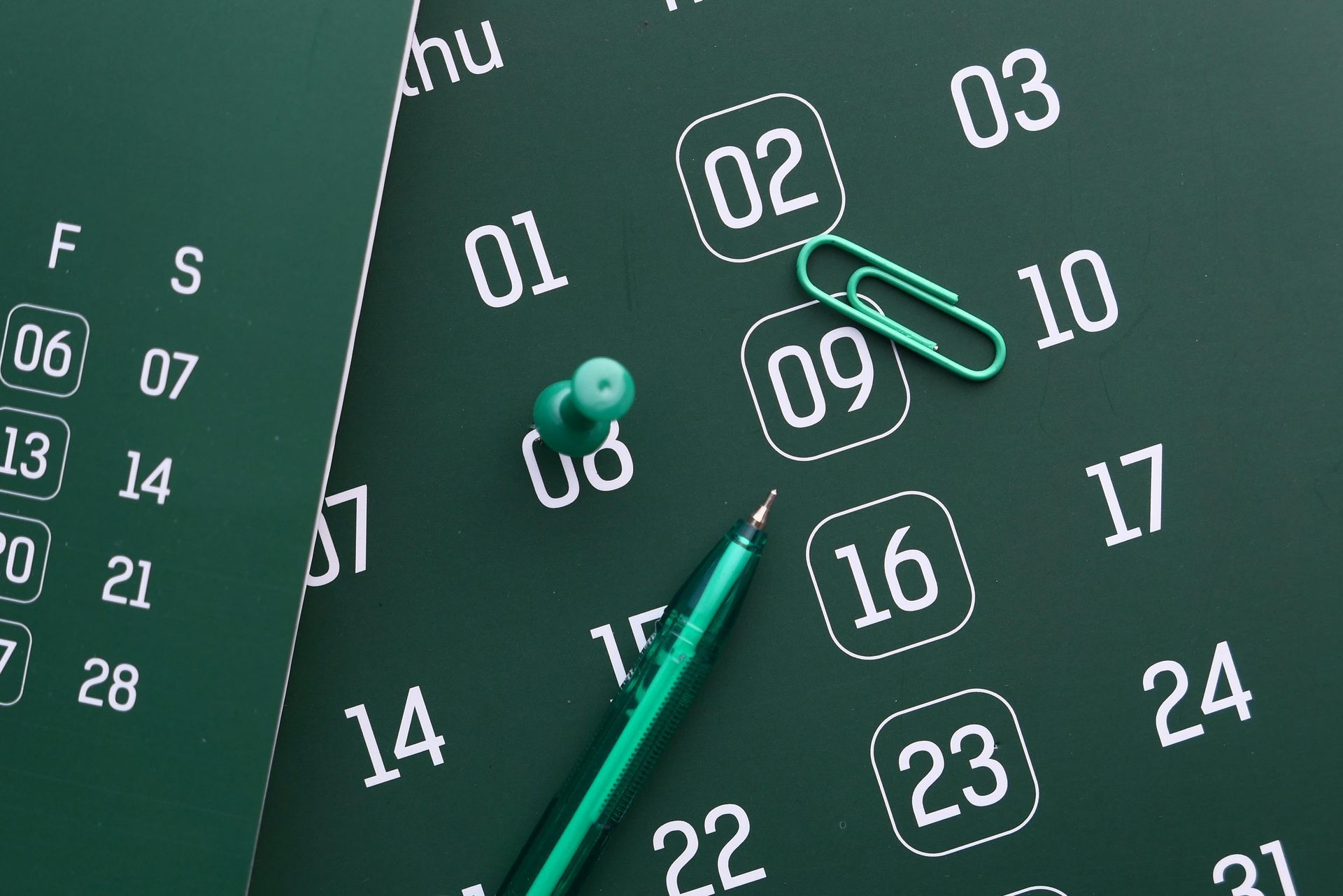 Green calendar with a pen, pushpin, and paper clip marking specific dates.
