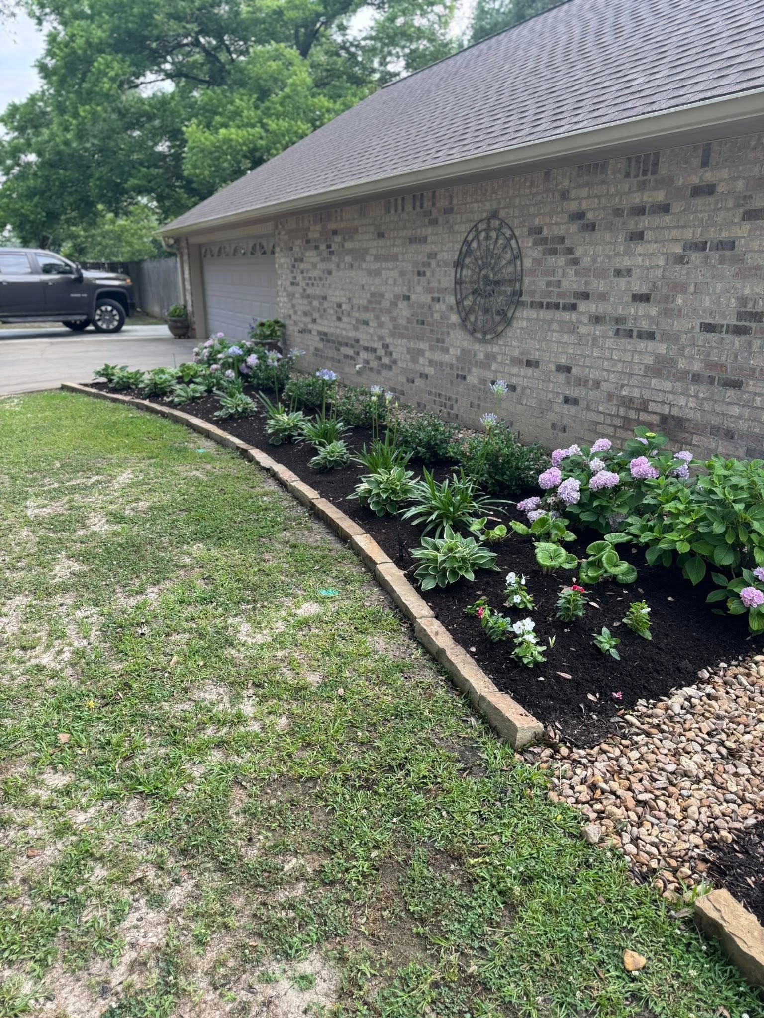 Lush garden bed with pink hydrangeas, brick wall, and a garage.
