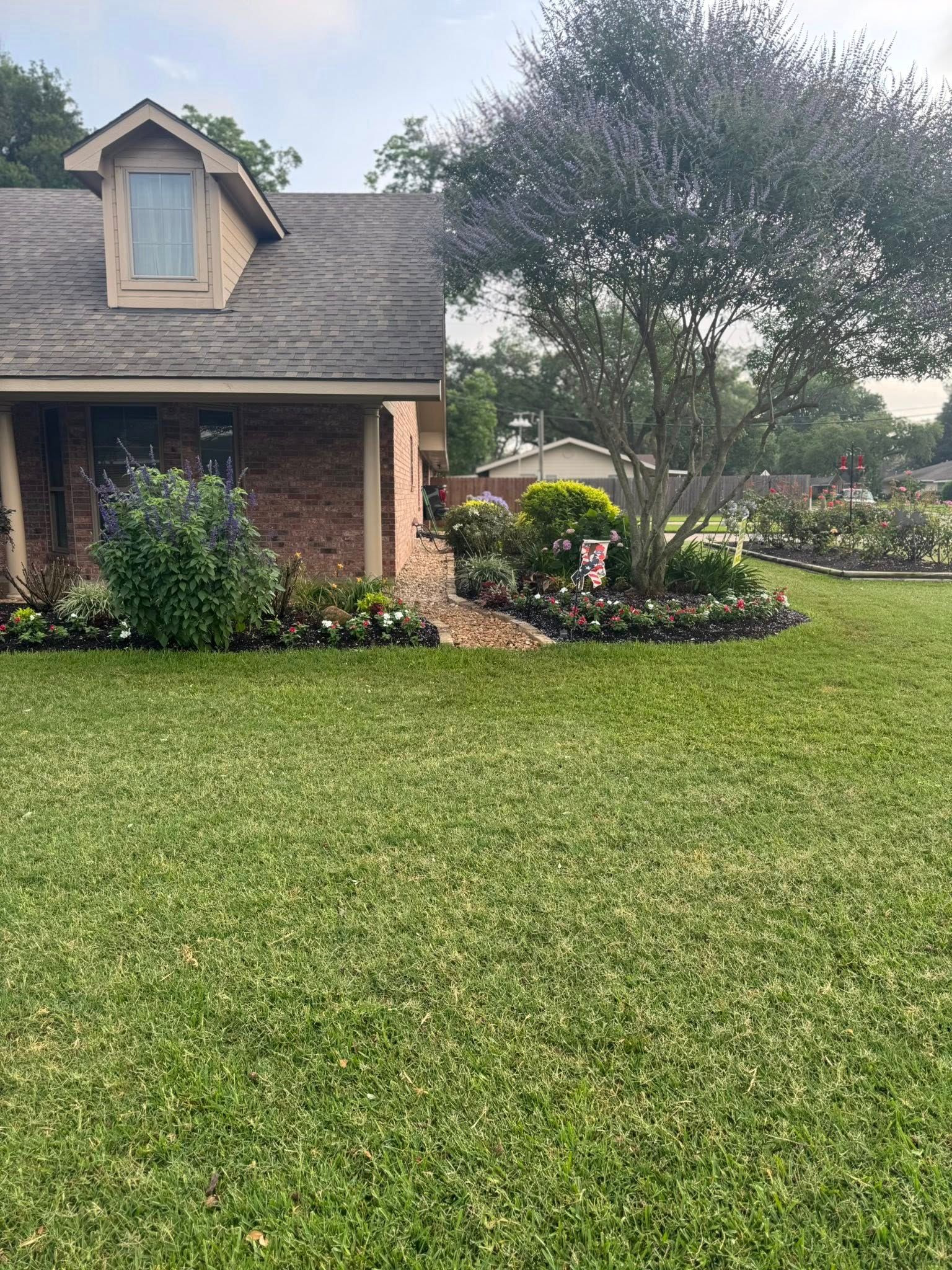 Brick house with a lush green lawn and colorful flower beds.