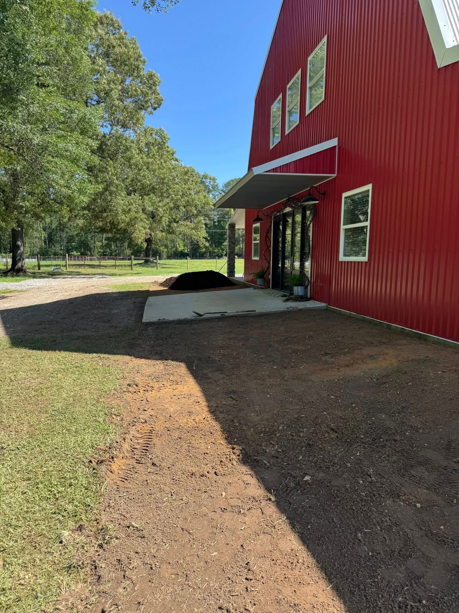 Red barn with gravel path, patio, and awning on a sunny day.