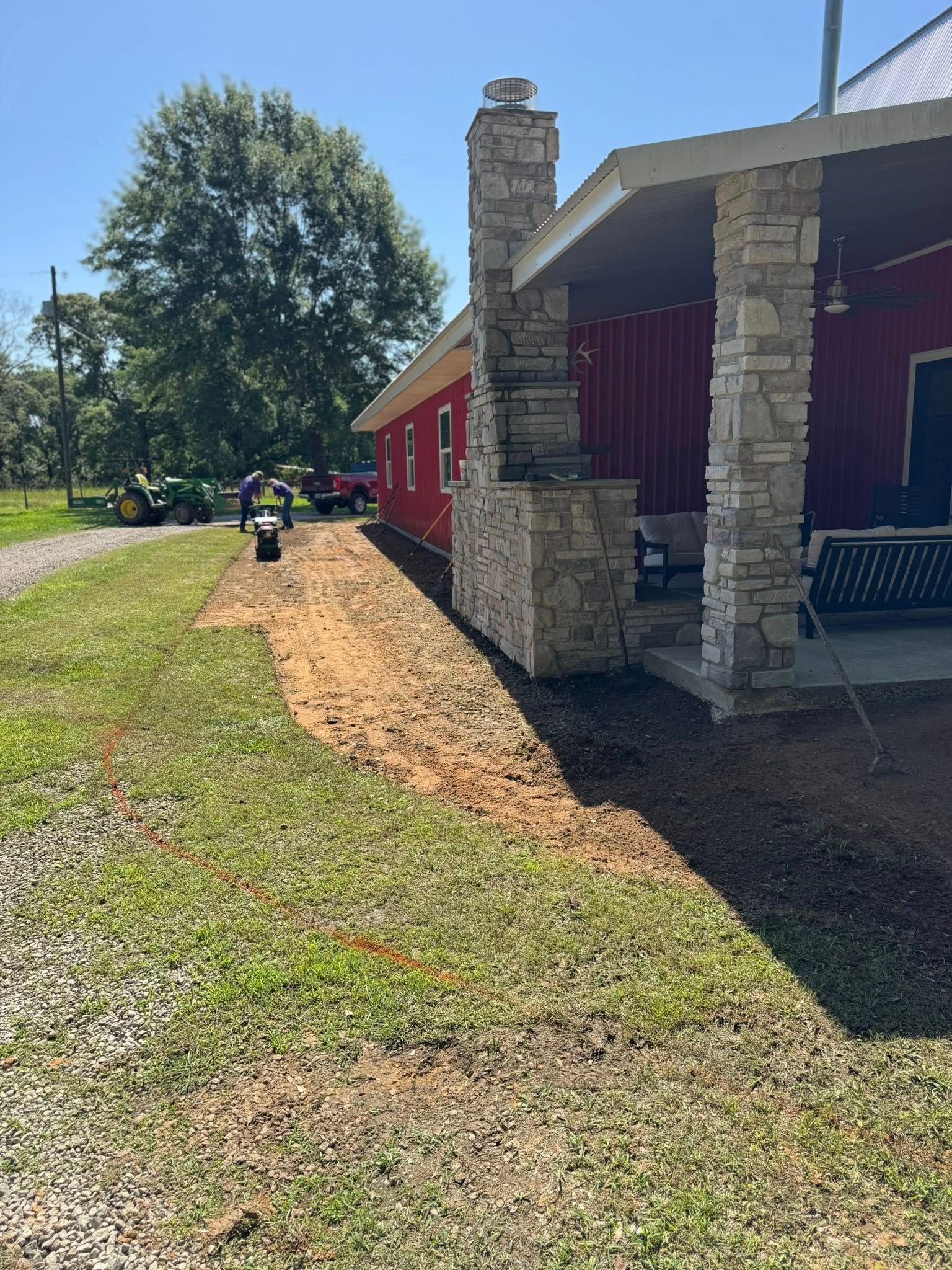 Red building with stone chimney and porch; dirt area next to the building and grass.