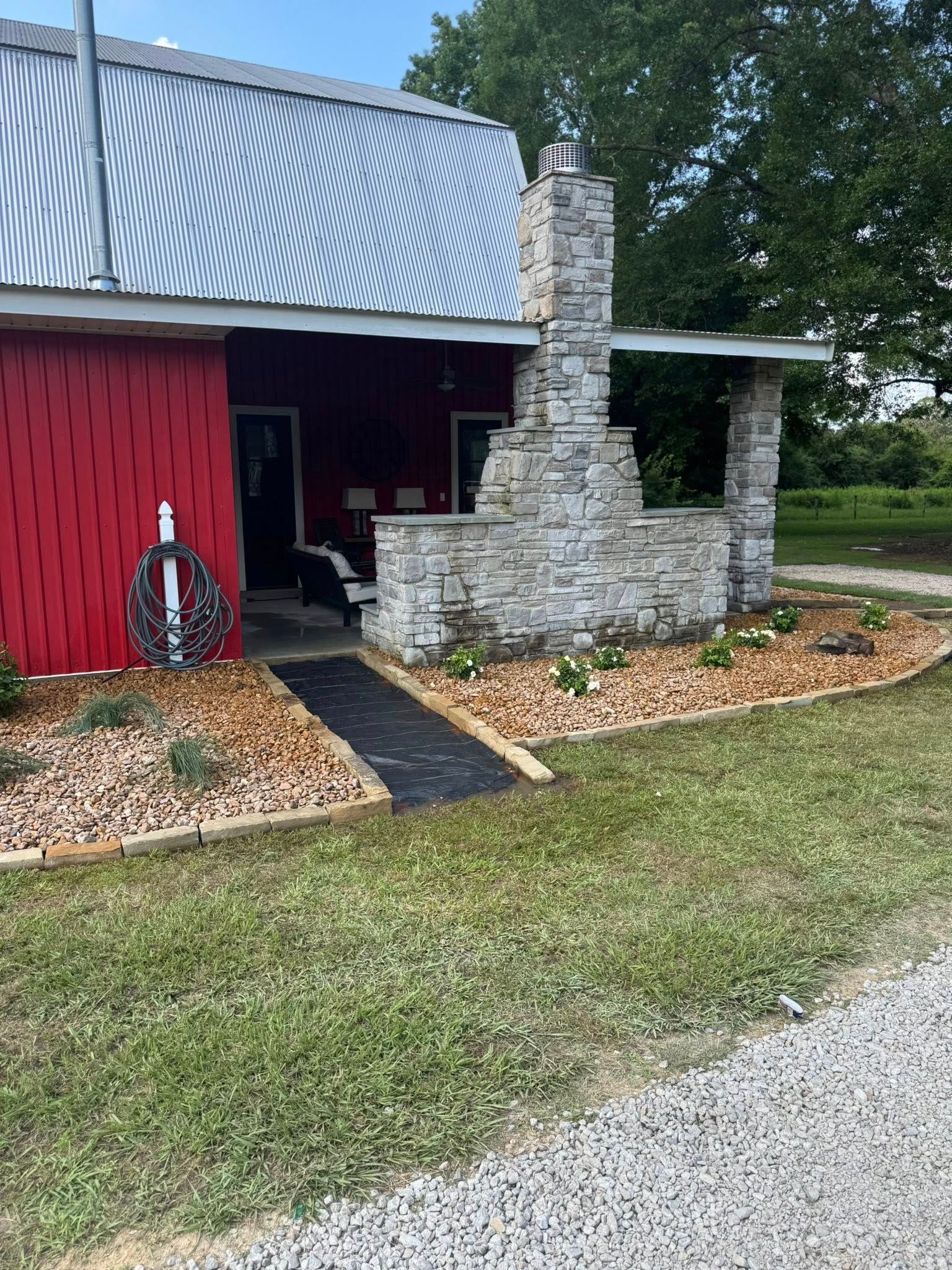 Red building with stone chimney and patio, bordered by mulch and flowers.