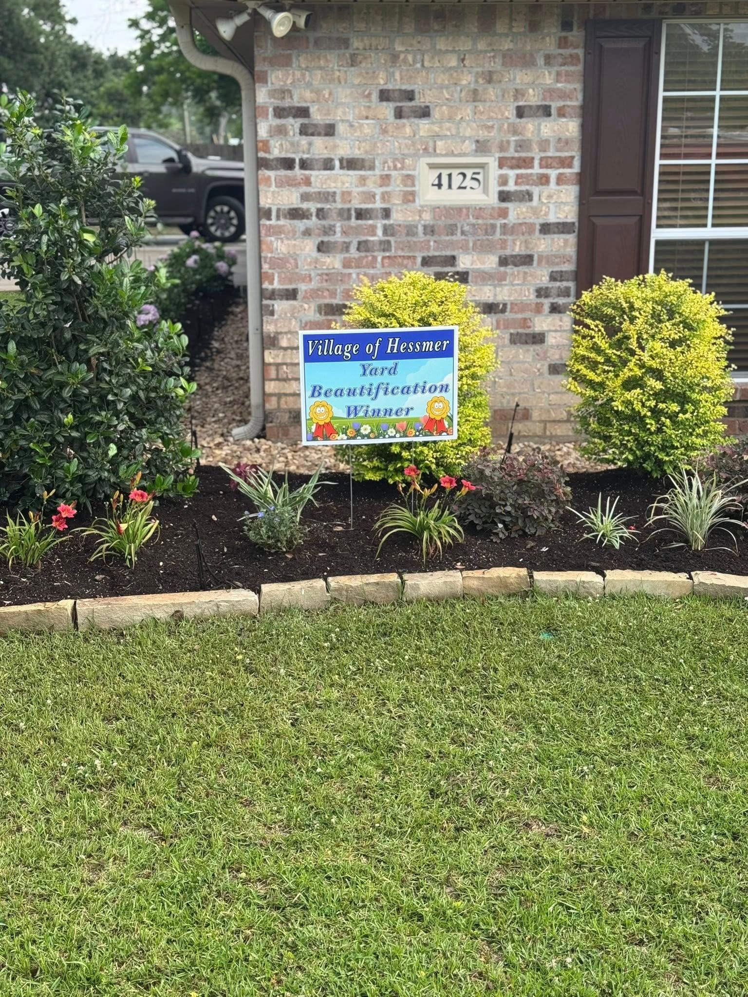 A house front with a welcome sign in a flower bed. The sign has cartoon images and a message.