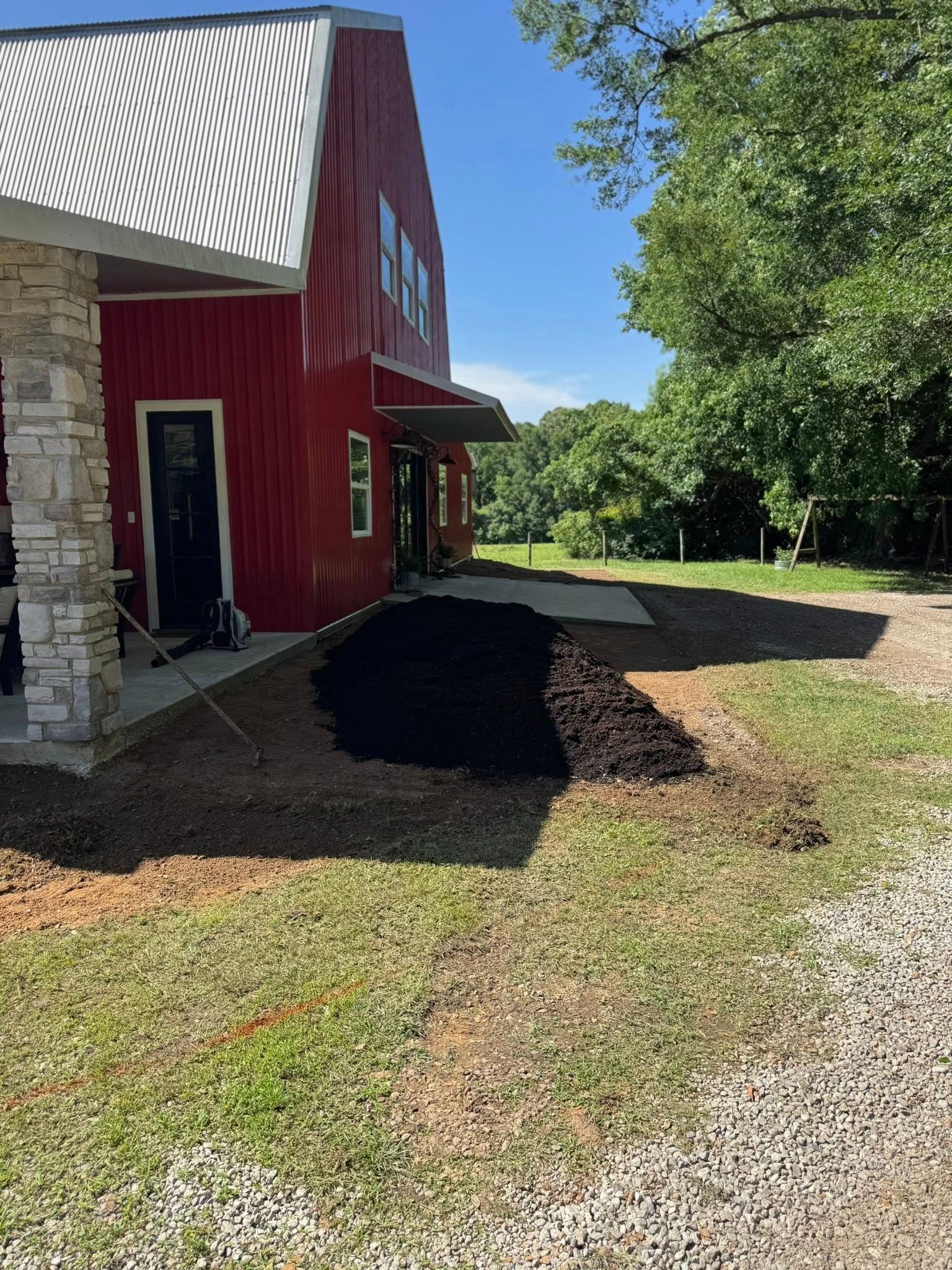 Red barn-style building with stone pillars and a dark mulch bed; a sunny day.